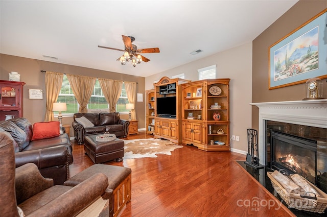 living room featuring a ceiling fan, a glass covered fireplace, wood finished floors, and baseboards