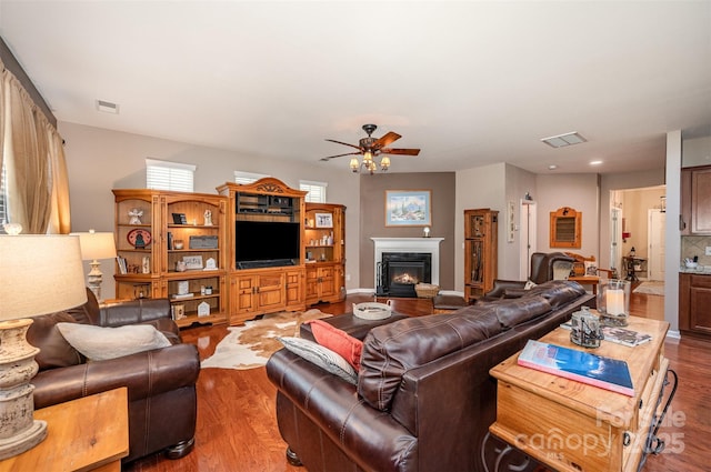living area featuring a ceiling fan, a lit fireplace, and wood finished floors
