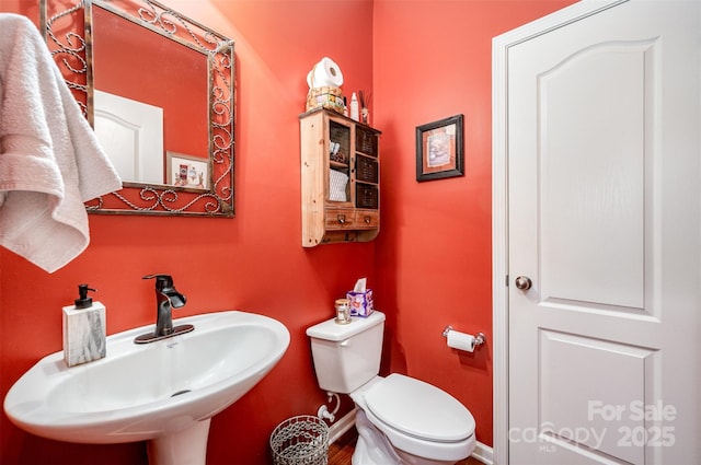 half bath with a sink, baseboards, toilet, and wood finished floors