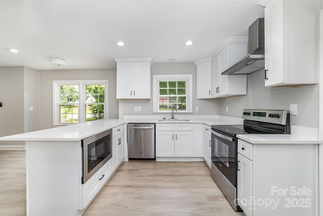 3920 Admiral Ave, Charlotte, NC 28205 - kitchen with appliances with stainless steel finishes, wall chimney exhaust hood, a sink, a peninsula, and light wood-type flooring
