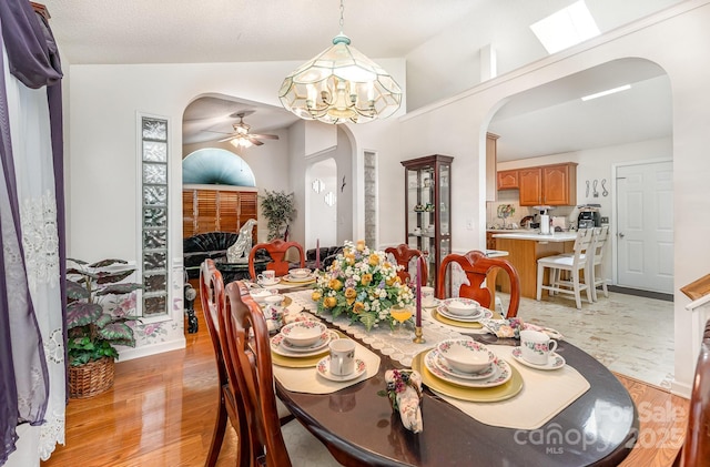 dining space featuring arched walkways, a ceiling fan, and light wood-style floors