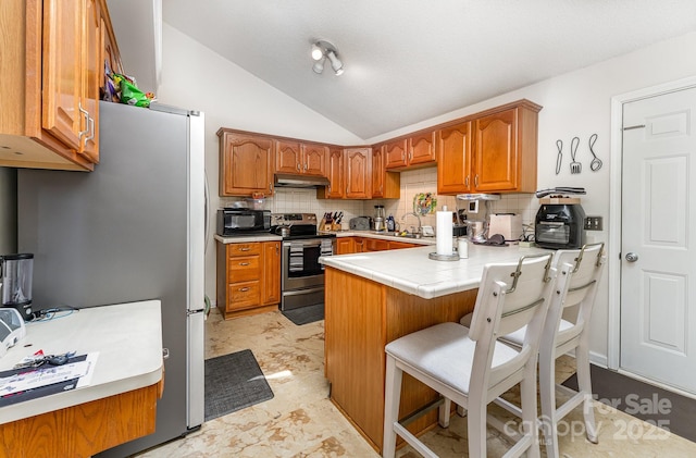 1076 Braxton Dr, Concord, NC 28025 - kitchen with stainless steel appliances, under cabinet range hood, a peninsula, brown cabinets, and decorative backsplash