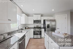 kitchen with stainless steel appliances, a sink, a center island, white cabinets, and stone counters