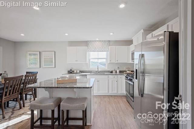 kitchen featuring stainless steel appliances, a sink, a kitchen island, a kitchen breakfast bar, and dark stone countertops