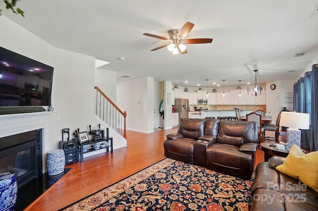 14316 Baytown Ct, Huntersville, NC 28078 - living area featuring stairway, light wood-style floors, a ceiling fan, a fireplace with flush hearth, and baseboards