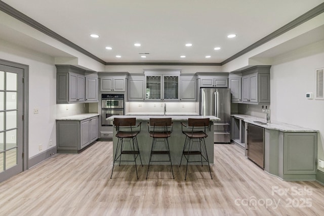 4920 Parview Dr S, Charlotte, NC 28226 - kitchen with gray cabinets, appliances with stainless steel finishes, ornamental molding, a kitchen island with sink, and light wood-style floors