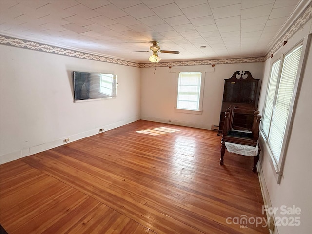 unfurnished living room featuring crown molding, light wood-type flooring, a baseboard heating unit, a ceiling fan, and baseboards