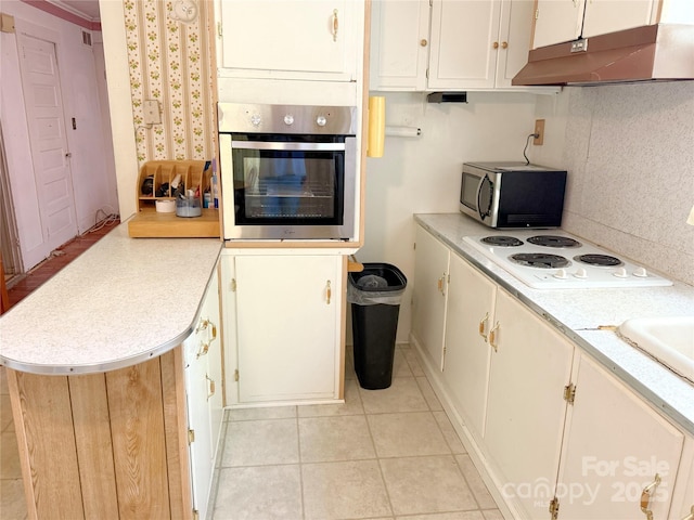 kitchen with stainless steel appliances, under cabinet range hood, light countertops, a peninsula, and light tile patterned flooring