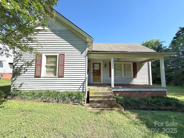 view of front of property with a front yard, covered porch, and a shingled roof