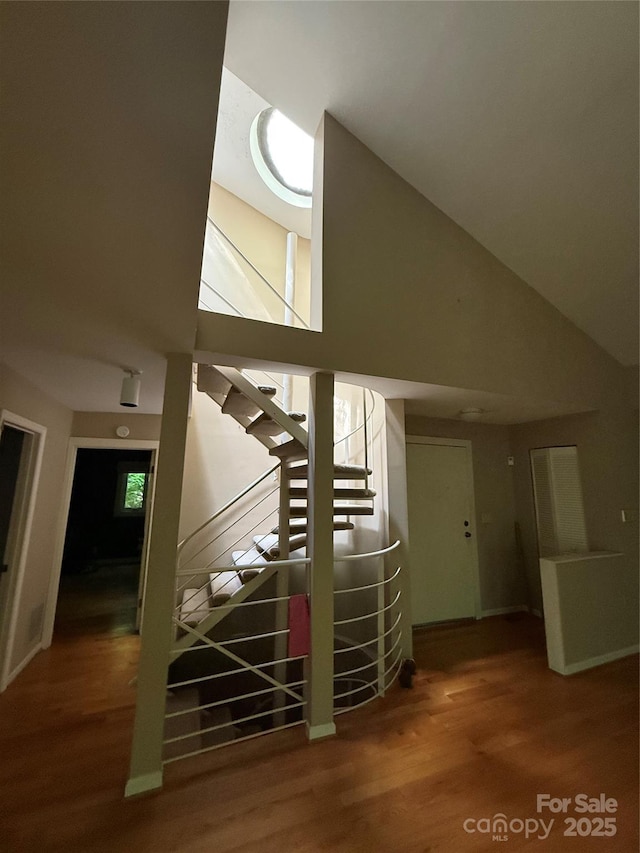 staircase featuring high vaulted ceiling, wood finished floors, and baseboards