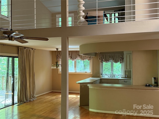 kitchen featuring light wood-style flooring, a sink, baseboards, ceiling fan, and a high ceiling