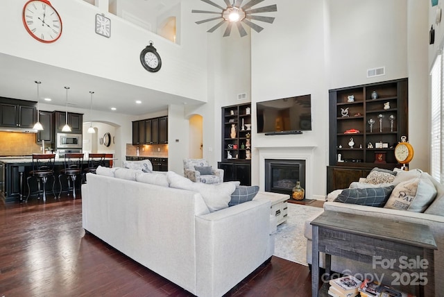 161 Leaning Tower Dr, Mooresville, NC 28117 - living area with arched walkways, ceiling fan, a towering ceiling, a glass covered fireplace, and dark wood-style floors