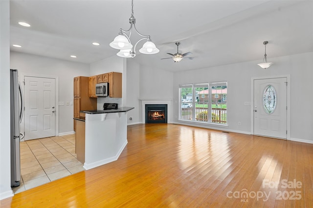 kitchen with appliances with stainless steel finishes, dark countertops, brown cabinets, a ceiling fan, and decorative light fixtures