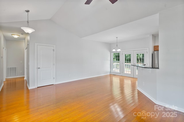 unfurnished living room featuring ceiling fan, light wood finished floors, baseboards, vaulted ceiling, and a chandelier