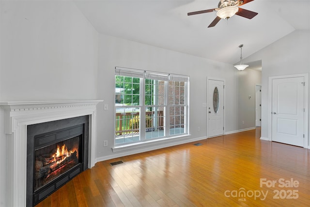 unfurnished living room with ceiling fan, wood finished floors, a lit fireplace, baseboards, and high vaulted ceiling