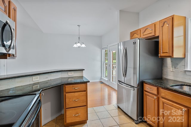 kitchen featuring appliances with stainless steel finishes, decorative backsplash, brown cabinetry, dark stone countertops, and light tile patterned floors