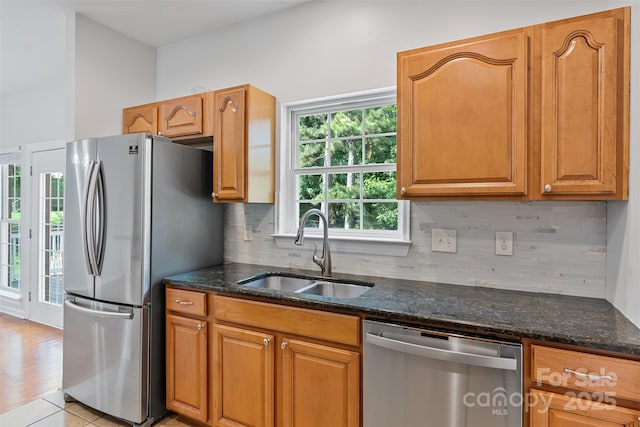 kitchen featuring stainless steel appliances, a sink, dark stone counters, decorative backsplash, and brown cabinets