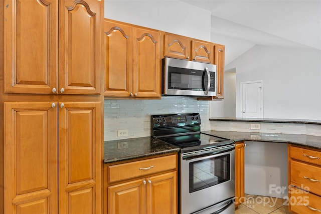 kitchen featuring appliances with stainless steel finishes, decorative backsplash, dark stone countertops, brown cabinetry, and lofted ceiling