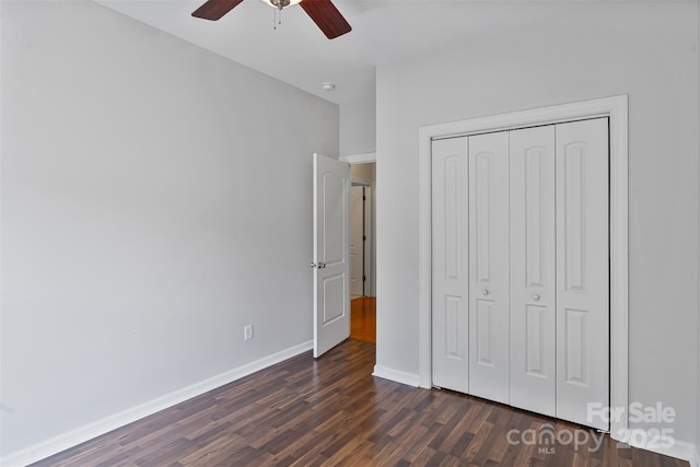 unfurnished bedroom with dark wood-style flooring, a closet, baseboards, and ceiling fan