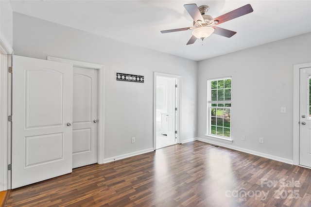 unfurnished bedroom with dark wood-style flooring, baseboards, ensuite bath, and a ceiling fan