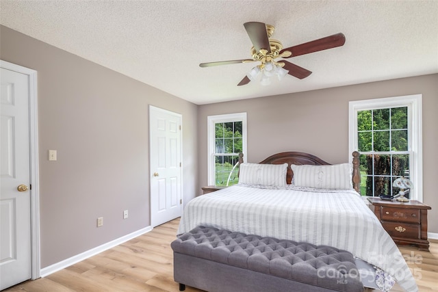 bedroom featuring multiple windows, light wood finished floors, baseboards, and a textured ceiling