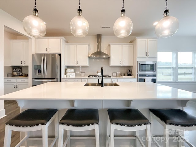 kitchen featuring appliances with stainless steel finishes, wall chimney range hood, backsplash, and white cabinets