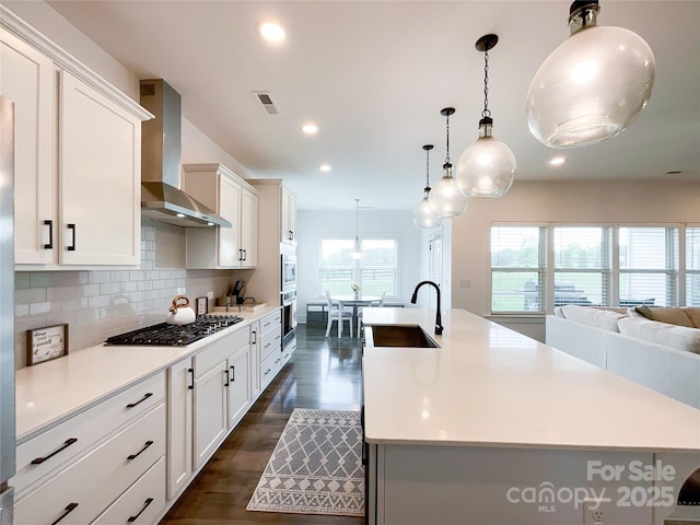 kitchen featuring a sink, wall chimney exhaust hood, appliances with stainless steel finishes, light countertops, and recessed lighting