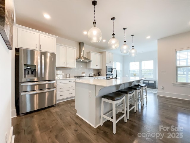 kitchen featuring appliances with stainless steel finishes, wall chimney exhaust hood, an island with sink, white cabinets, and recessed lighting