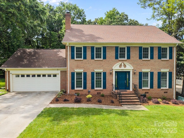 colonial home featuring a chimney, an attached garage, concrete driveway, a front yard, and brick siding
