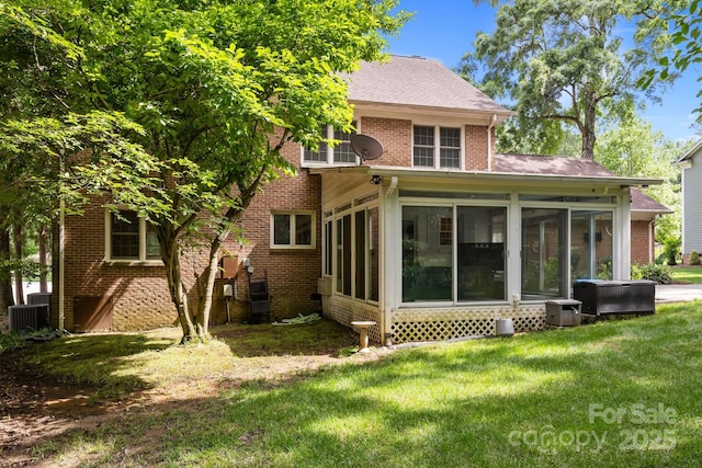 rear view of house with a sunroom, central air condition unit, a lawn, and brick siding