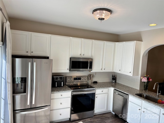 kitchen with stainless steel appliances, a sink, arched walkways, light stone countertops, and backsplash