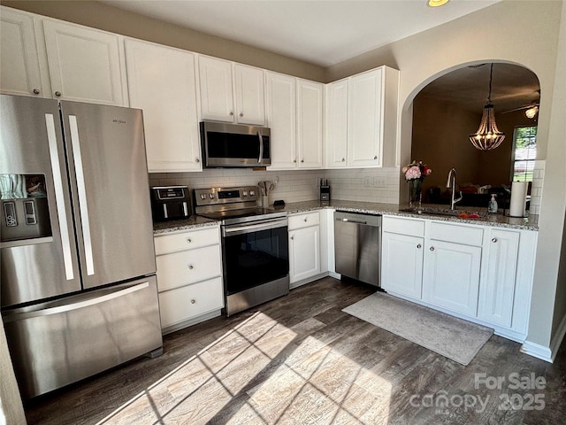 kitchen featuring appliances with stainless steel finishes, a sink, dark wood-style flooring, white cabinets, and decorative backsplash