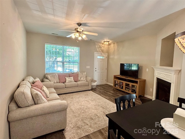 living area with dark wood finished floors, a ceiling fan, a fireplace, and baseboards