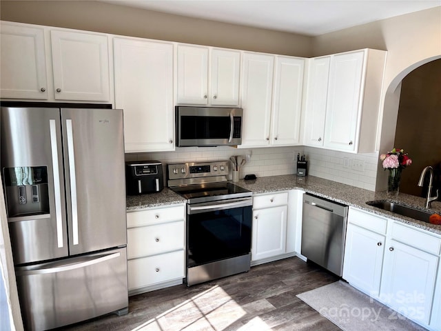 kitchen featuring stainless steel appliances, a sink, arched walkways, dark wood finished floors, and white cabinetry
