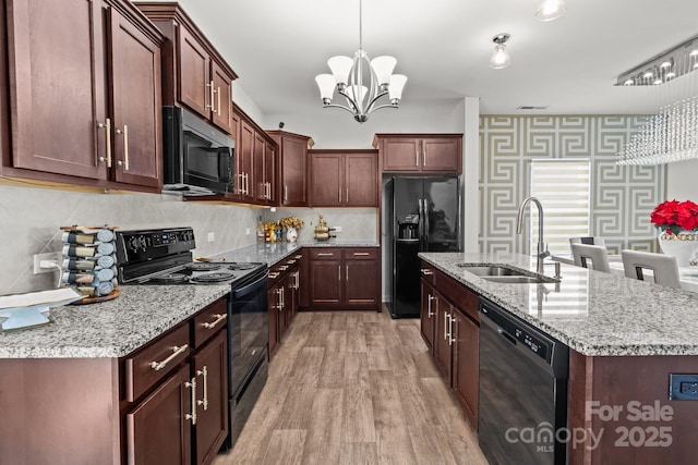 9132 Colwick Hill Ln, Charlotte, NC 28215 - kitchen with black appliances, a sink, wallpapered walls, light wood-style floors, and an island with sink