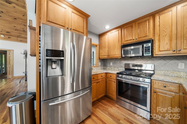 332 Mystic Cv, Waynesville, NC 28785 - kitchen featuring appliances with stainless steel finishes, light wood finished floors, tasteful backsplash, light stone counters, and brown cabinets