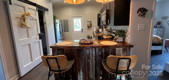 bar area with dark wood-style flooring, stainless steel appliances, a barn door, and decorative backsplash