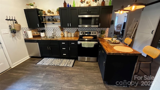 kitchen featuring appliances with stainless steel finishes, a sink, dark cabinets, butcher block countertops, and backsplash