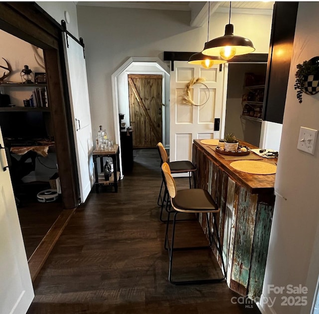 bar area with a barn door, dark wood-style floors, pendant lighting, beam ceiling, and a sink