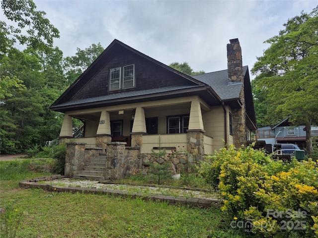 view of front of property with stone siding, covered porch, roof with shingles, and a chimney