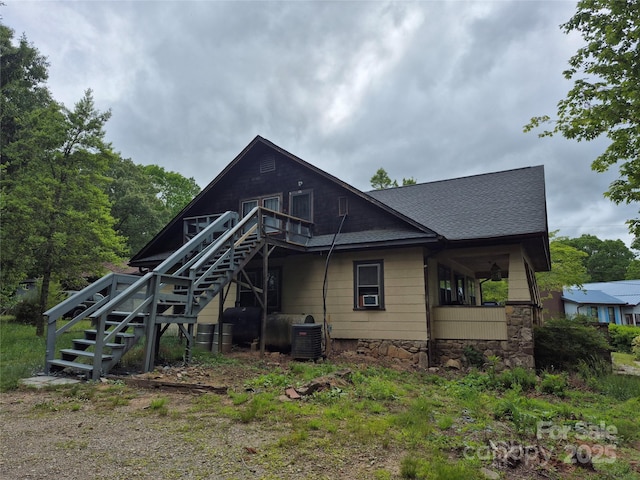 back of property with stairway, stone siding, roof with shingles, and cooling unit