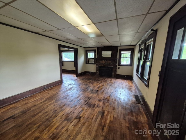 unfurnished living room featuring a paneled ceiling, a large fireplace, hardwood / wood-style flooring, baseboards, and healthy amount of natural light
