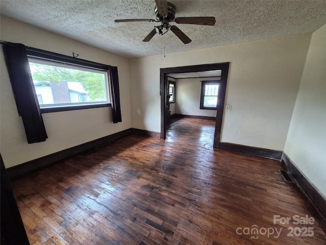 unfurnished room with a textured ceiling, a ceiling fan, dark wood-type flooring, and baseboards