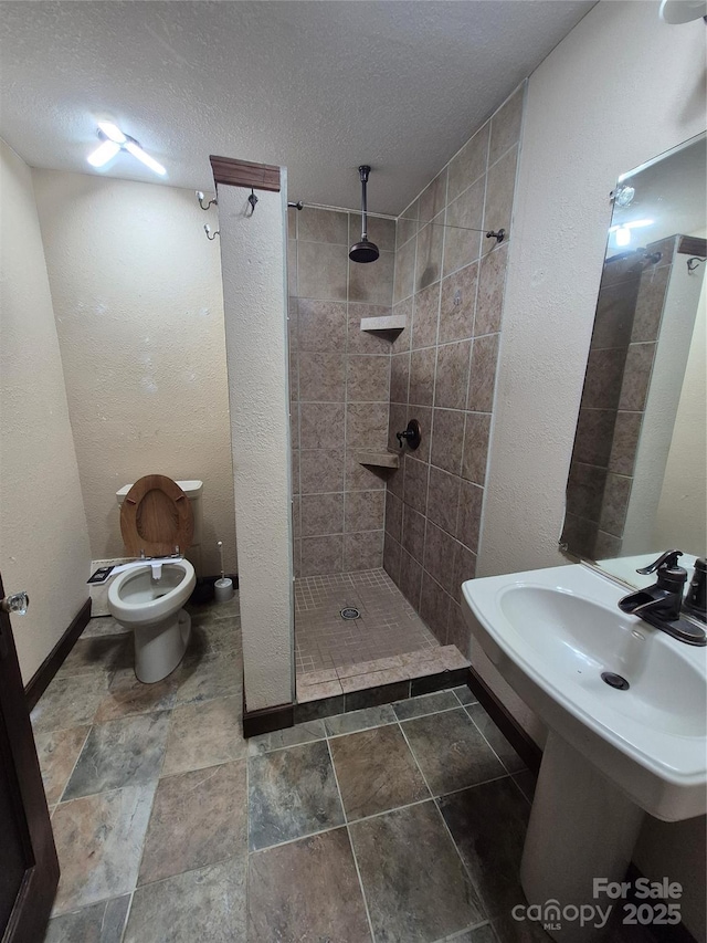 bathroom with a textured ceiling, tiled shower, a textured wall, baseboards, and toilet