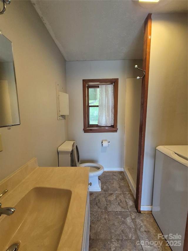 bathroom featuring toilet, a shower, baseboards, vanity, and stone finish flooring