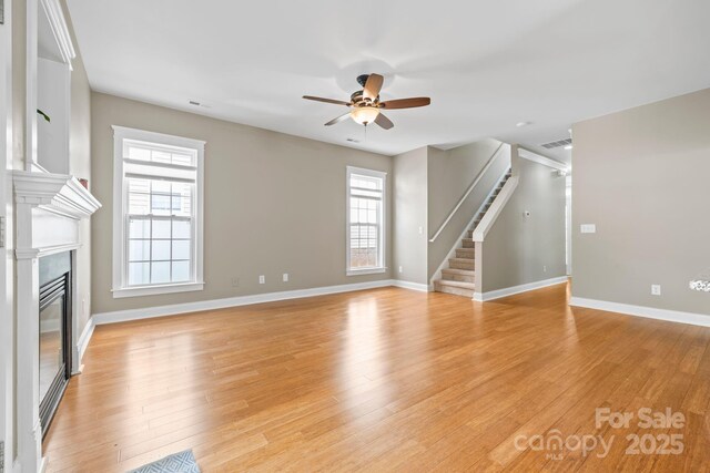 132 E Morehouse Ave, Mooresville, NC 28117 - unfurnished living room featuring a ceiling fan, a glass covered fireplace, stairway, baseboards, and light wood finished floors