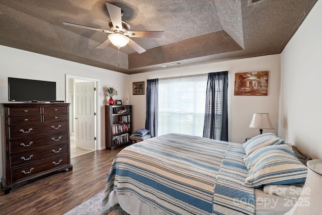 bedroom with dark wood-type flooring, a raised ceiling, ceiling fan, and a textured ceiling