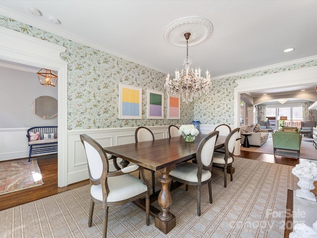dining area with wood finished floors, a chandelier, crown molding, and wainscoting