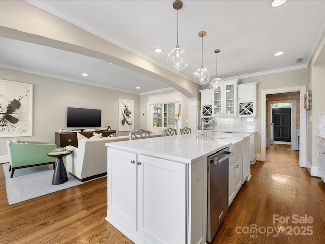 kitchen featuring dishwasher, arched walkways, an island with sink, white cabinets, and wood finished floors