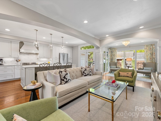living room featuring arched walkways, light wood finished floors, crown molding, and recessed lighting